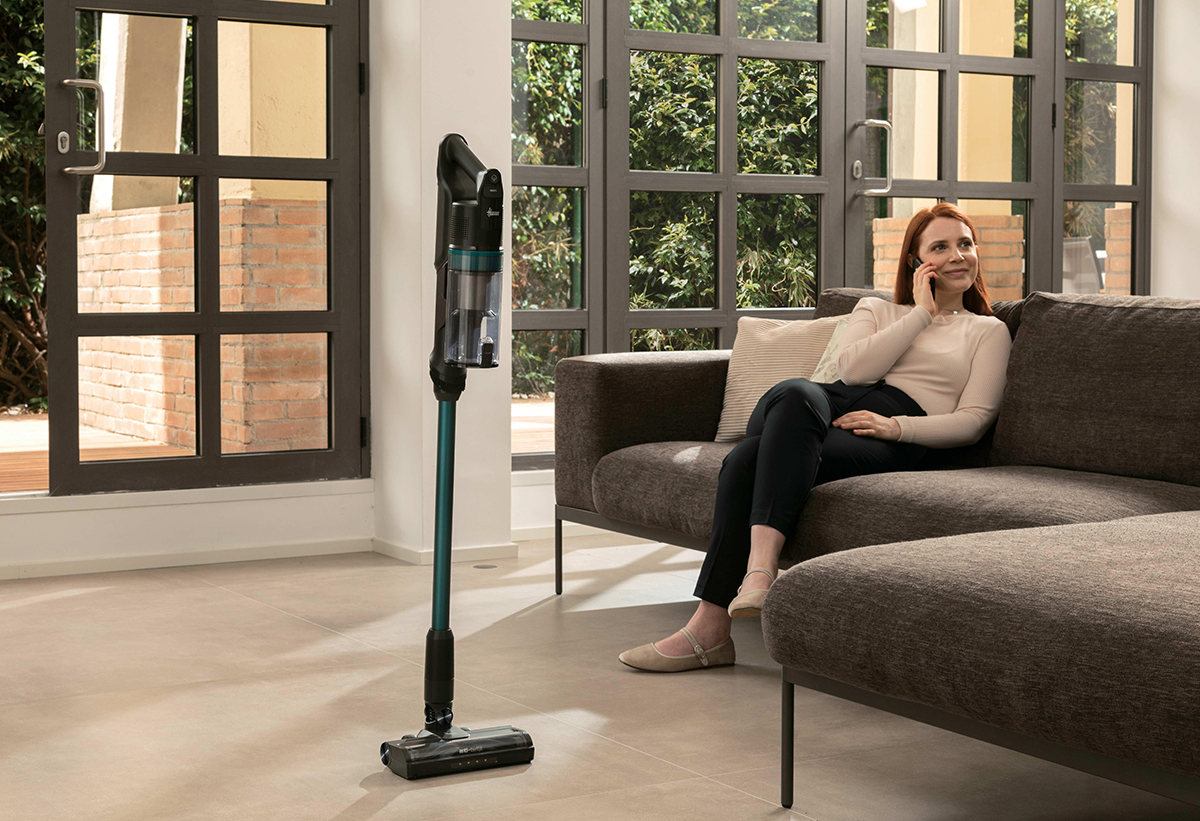 Μια γυναίκα είναι καθισμένη σε καναπέ ενώ η σκούπα καθεται όρθια στο κέντρο του σαλονιού.